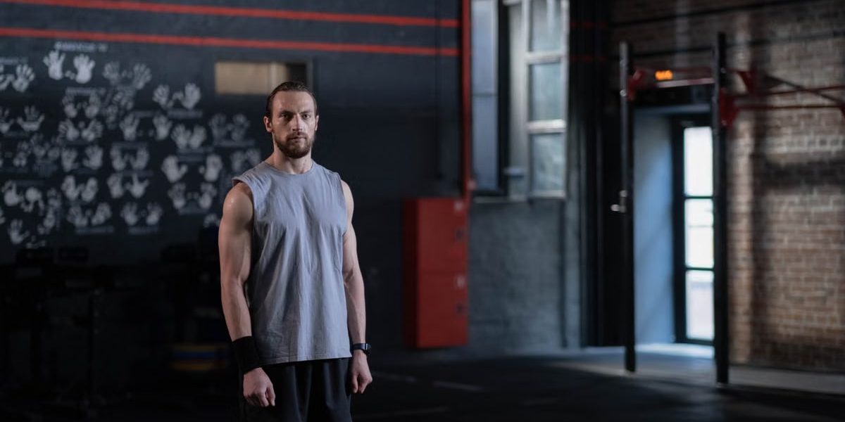 Muscular man standing in a gym with gymnastic rings, showcasing fitness and strength.