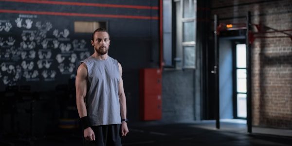Muscular man standing in a gym with gymnastic rings, showcasing fitness and strength.