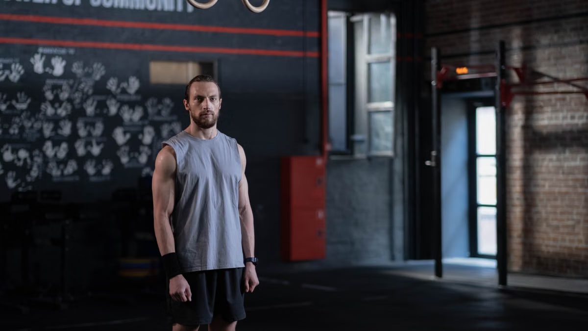 Muscular man standing in a gym with gymnastic rings, showcasing fitness and strength.